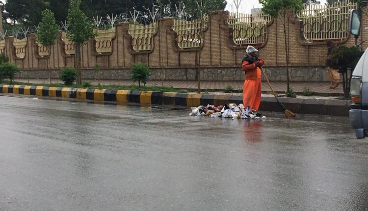 یک نارنجی پوش برای تنظیف شهر در زیر باران